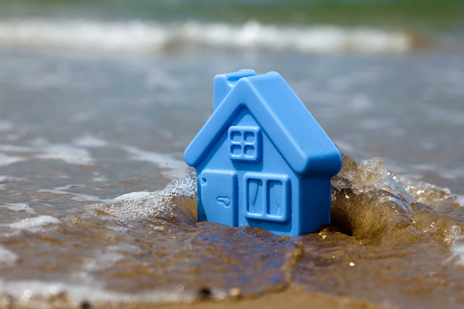 Blue toy plastic house on the sand washes wave